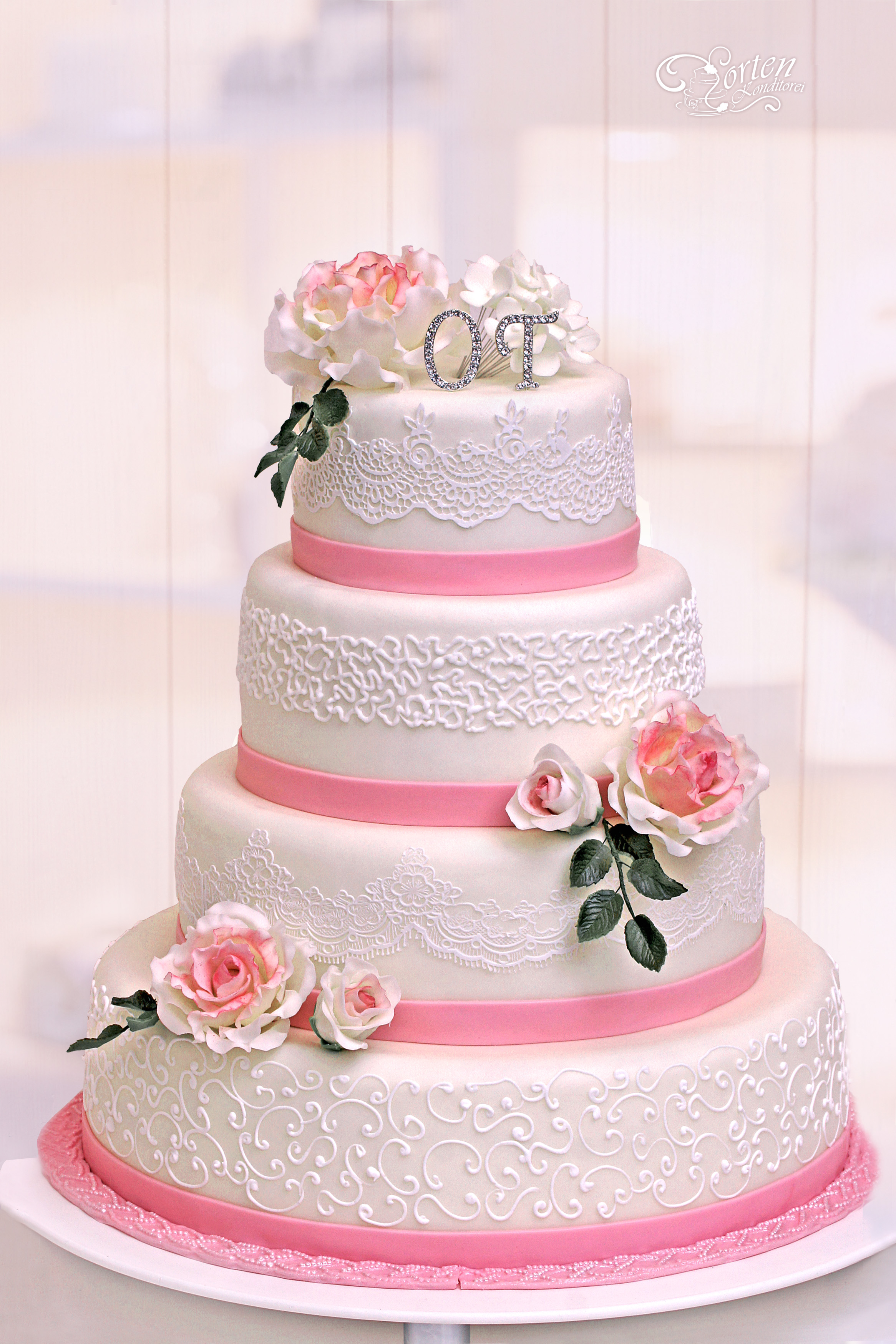 Hochzeitstorte mit Teerosen, Spitze und Schnörkeln in rosa-weiß und etwas grün.