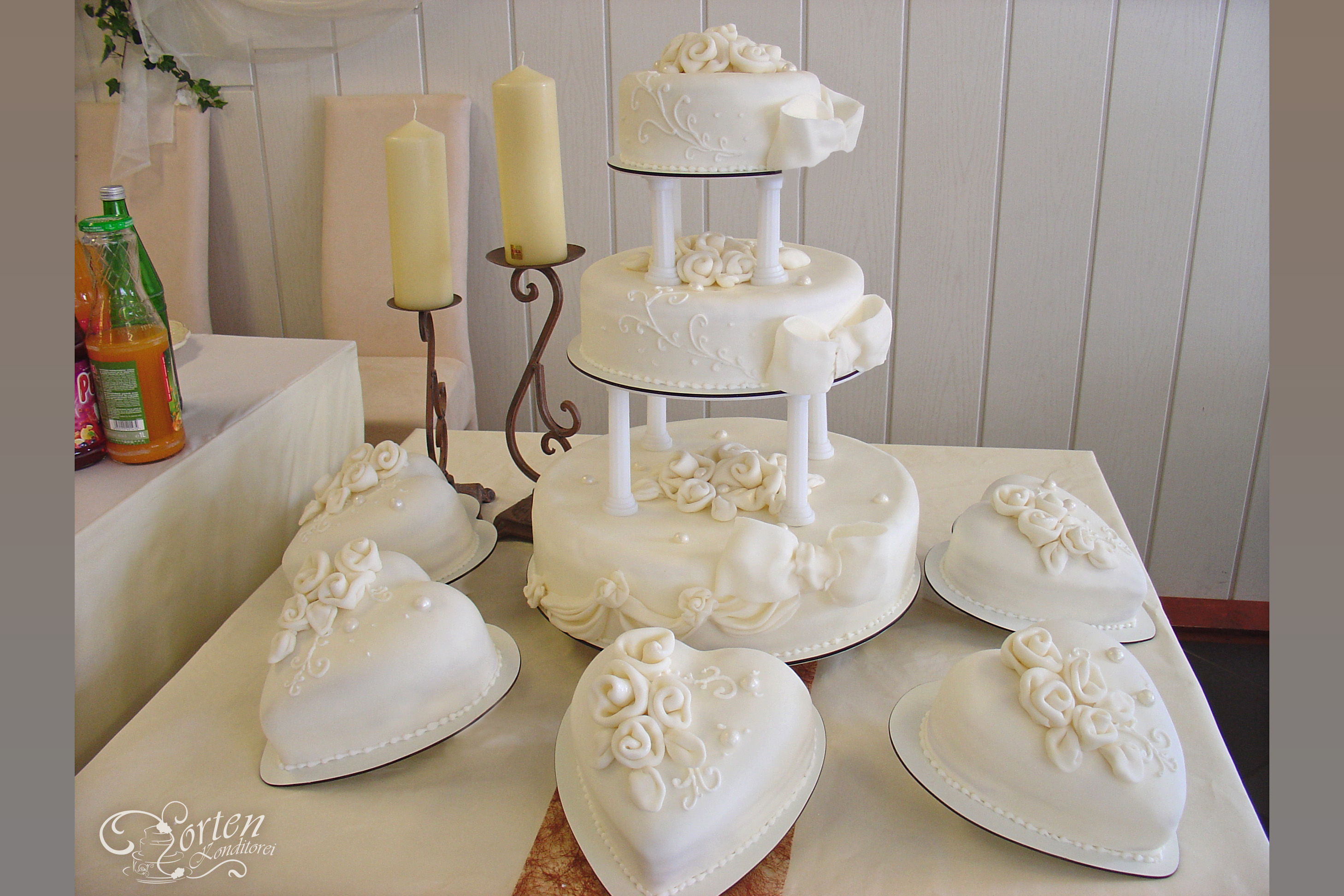 Sehr elegante, weiße zarte Hochzeitstorte, die zu jeder Hochzeitsdekoration passt. Die Torten sind gedeckt mit Fondant, weißen Rosen, Perlen, Schleifen und verziert mit einem Muster.