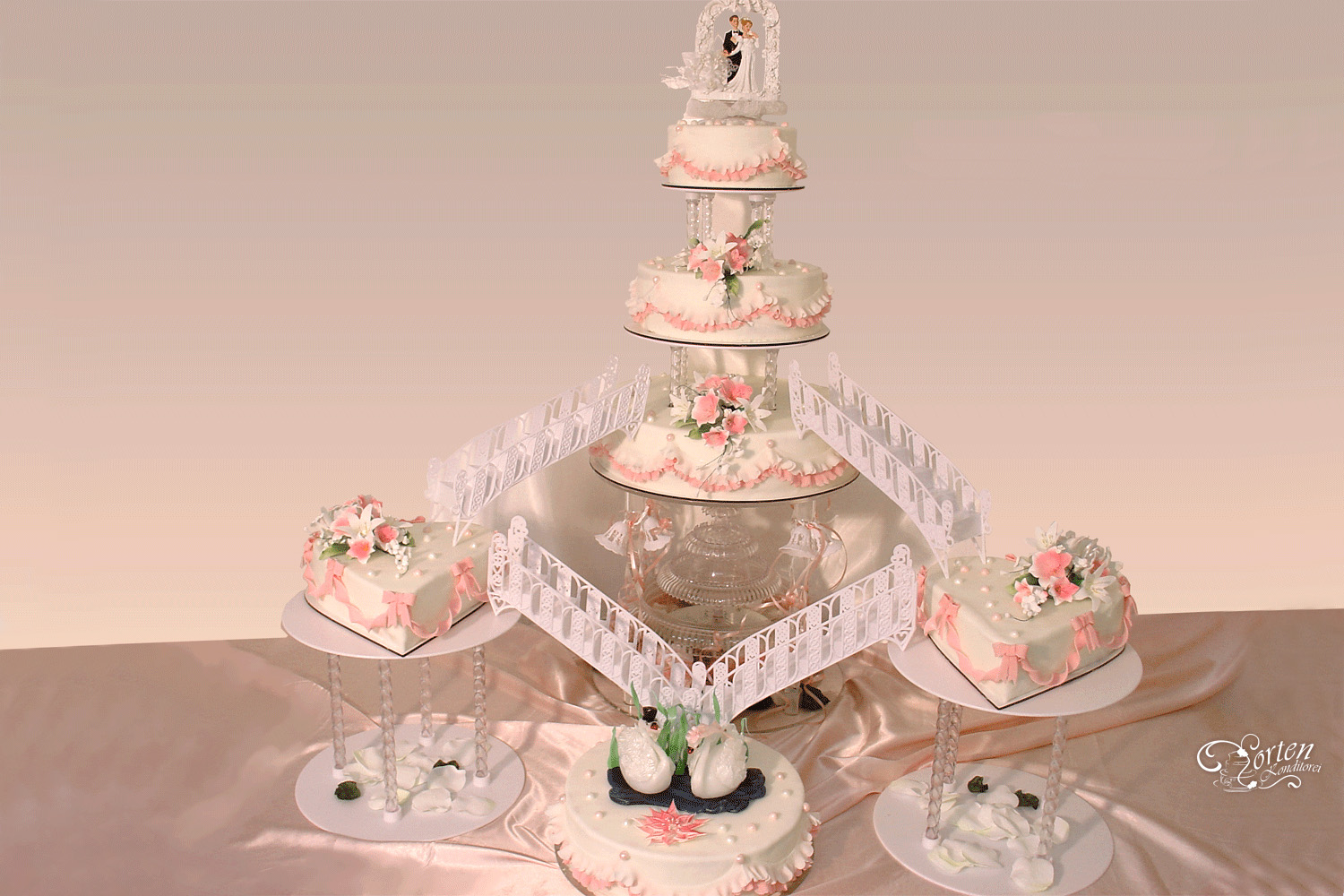 Sehr feierliche, rosa-weiße Hochzeits-Torte mit Wasserfall und Treppen. Dekoriert mit Blumenbuketts, Perlen, Schleifen und Rüschen. Unten sind handgefertigte Zucker-Schwaene.